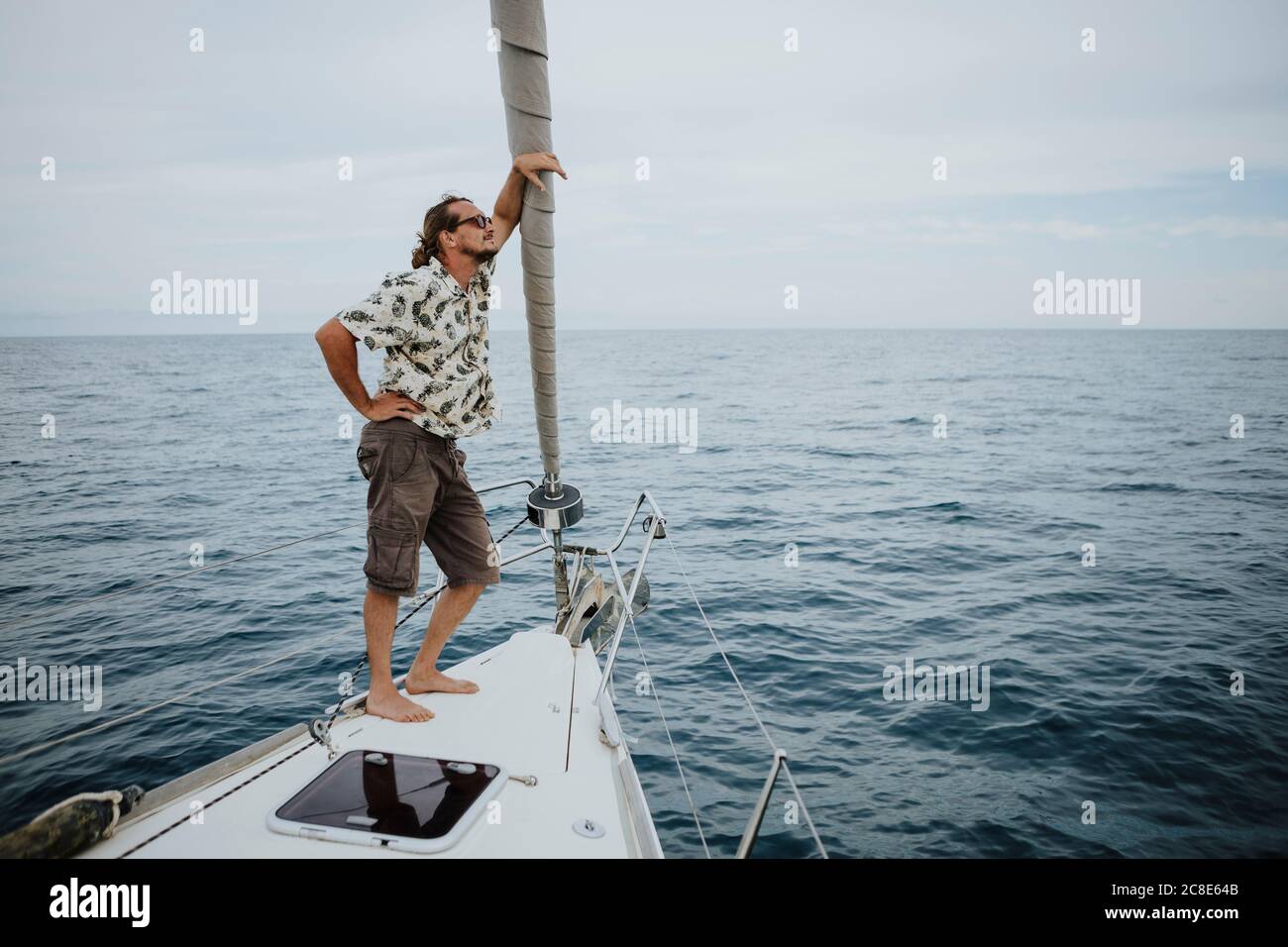 Marin mâle debout sur l'arc du voilier en mer contre ciel Banque D'Images