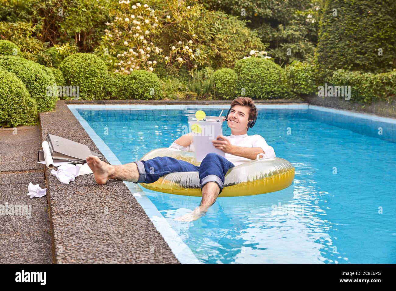 Jeune homme assis sur un matelas pneumatique dans la piscine et travaillant Banque D'Images