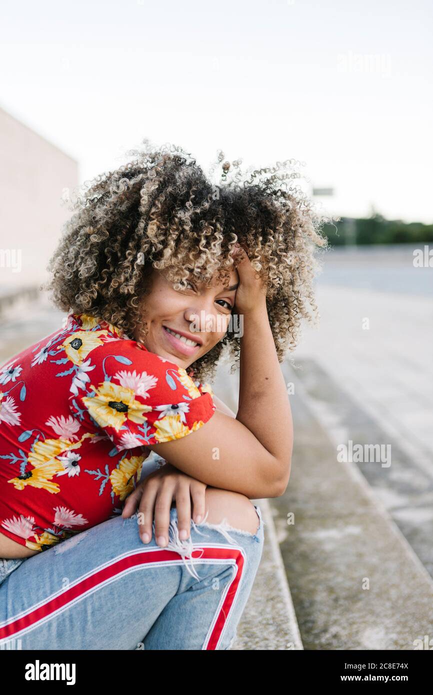 Bonne jeune femme assise avec la main dans les cheveux sur les marches par beau temps Banque D'Images