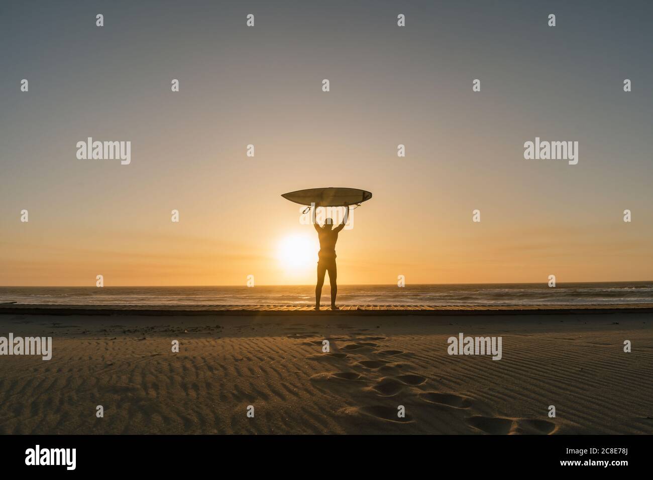 Surfeur tenant la planche de surf sur la plage, regardant le coucher du soleil Banque D'Images