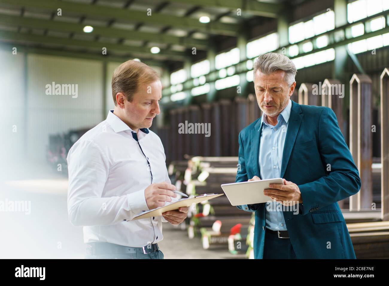 Homme d'affaires avec tablette et employé avec presse-papiers dans une usine Banque D'Images