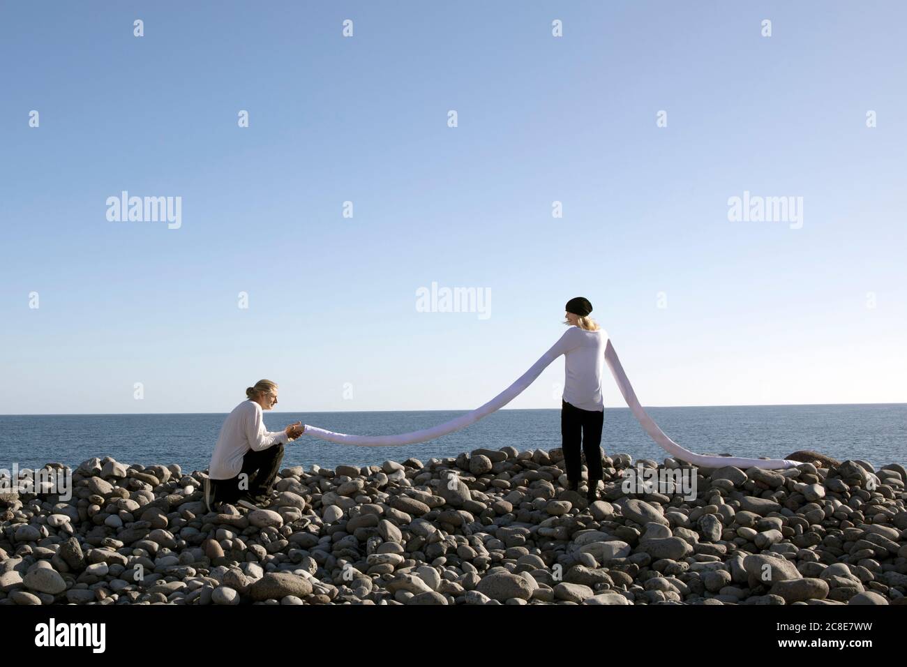 Homme proposant en tenant la longue main artificielle de la femme à la plage contre le ciel dégagé Banque D'Images