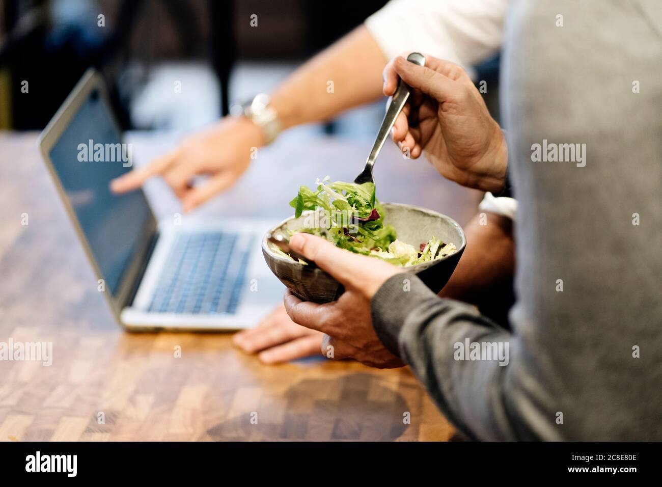 Homme tenant le bol avec la salade tandis que l'autre pointe vers ordinateur portable Banque D'Images