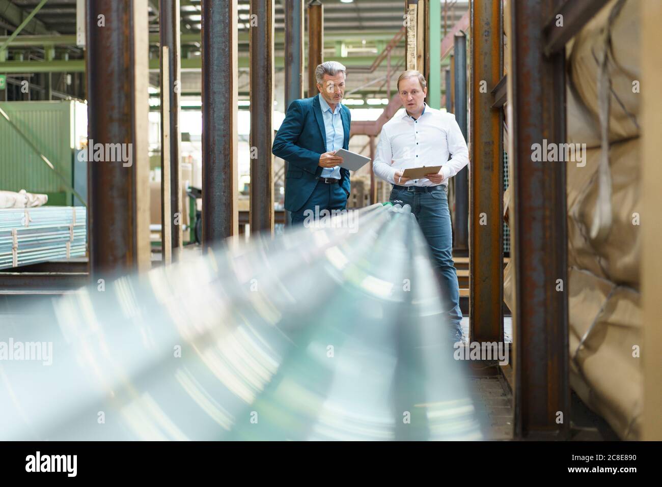 Homme d'affaires avec tablette et employé avec presse-papiers dans une usine Banque D'Images