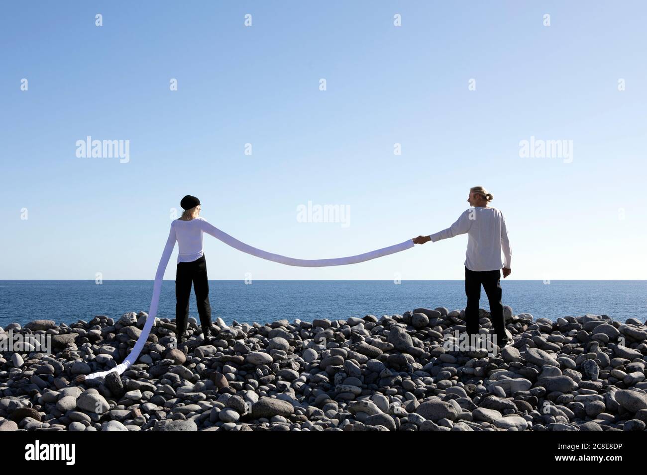 Femme avec de longs bras artificiels tenant la main de l'homme à la plage contre le ciel dégagé Banque D'Images