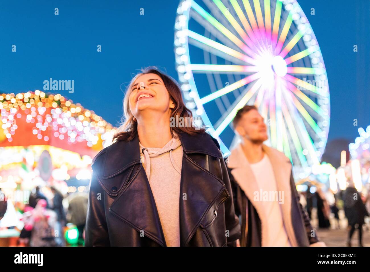 Jeune femme souriante avec petit ami appréciant dans le parc d'attractions à nuit Banque D'Images