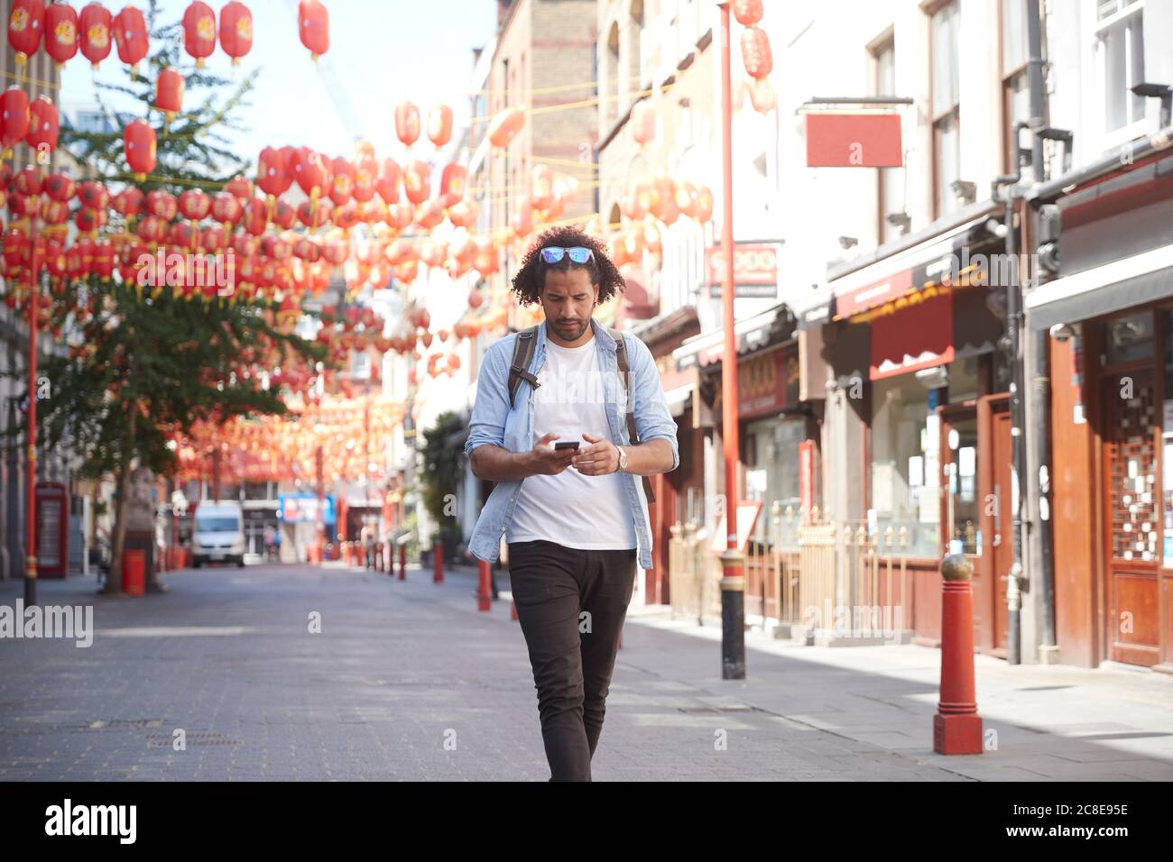 Jeune homme marchant dans la rue en regardant le smartphone, Chinatown, Londres, Royaume-Uni Banque D'Images