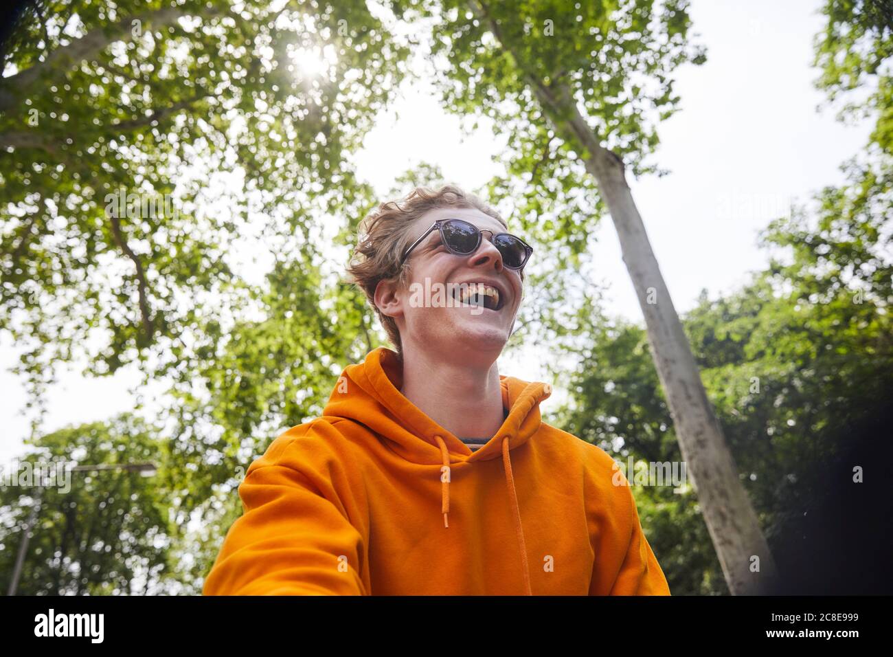 Portrait d'un jeune homme en train de rire portant des lunettes de soleil et un sweat à capuche orange chemise dans la nature Banque D'Images