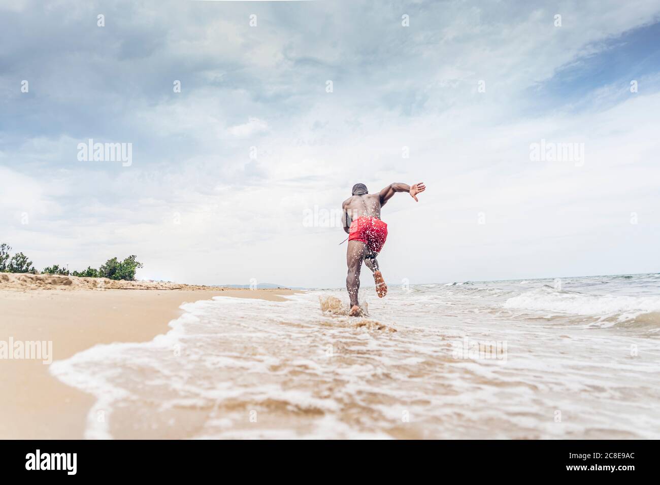 Vue arrière de l'homme sportif qui court sur la plage Banque D'Images