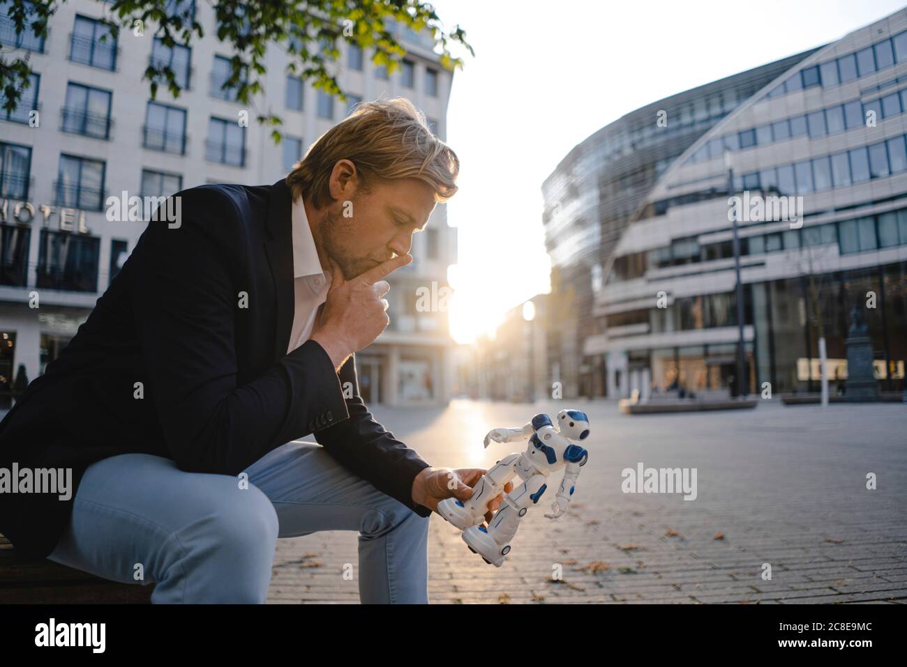 Homme d'affaires assis sur un banc dans la ville tenant mini robot Banque D'Images