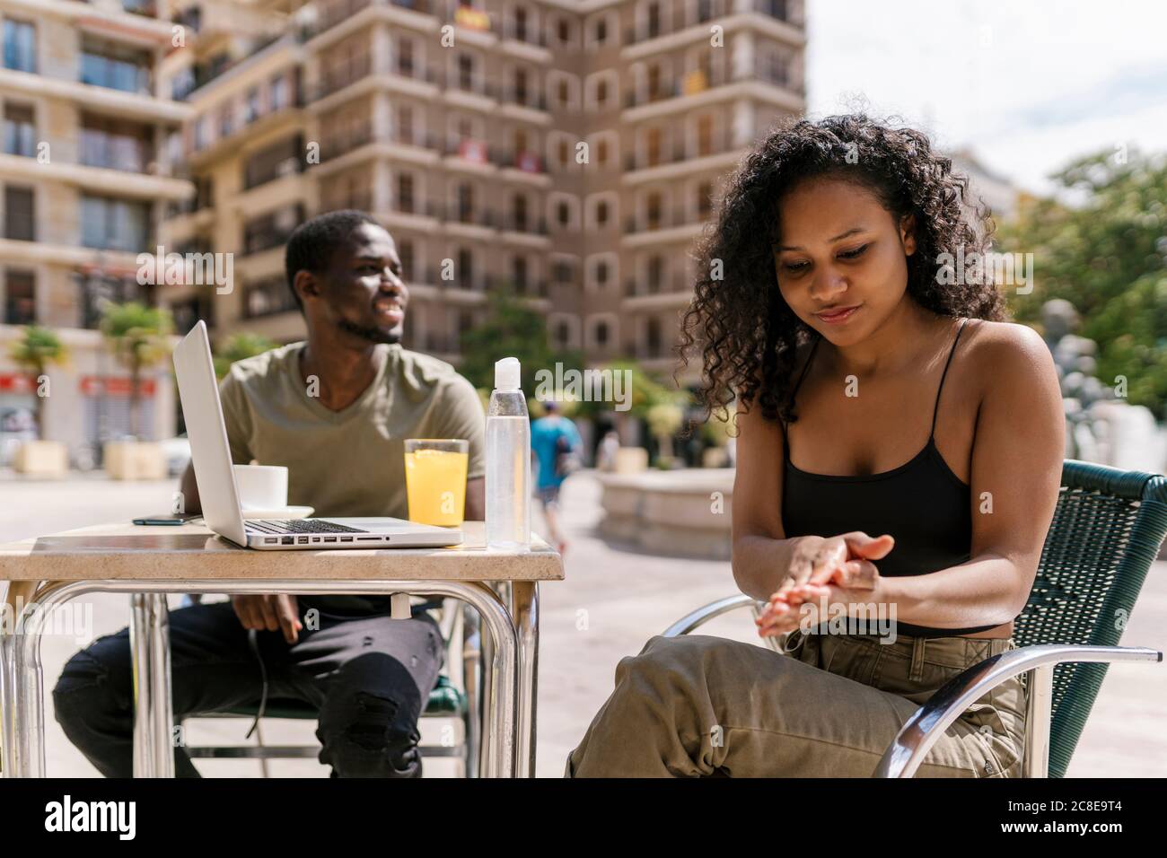 Une jeune femme se nettoie les mains avec de l'assainisseur pendant que l'homme est assis café-terrasse Banque D'Images