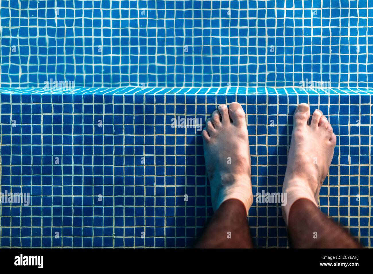 Pieds d'homme debout à la cheville dans la piscine Banque D'Images
