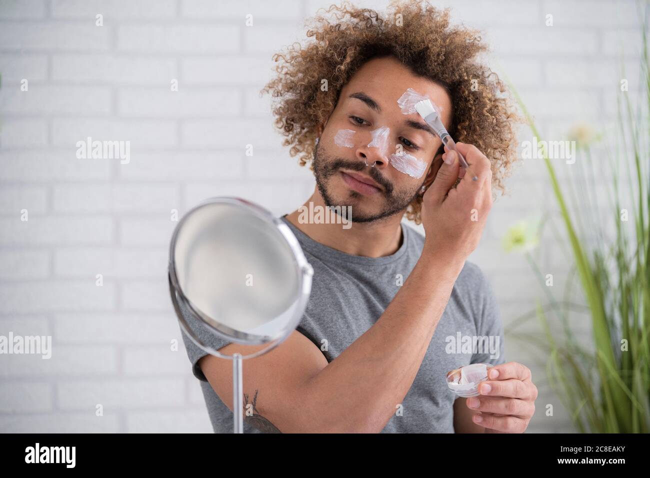Gros plan d'un jeune homme appliquant un masque facial tout en regardant dans miroir à la maison Banque D'Images