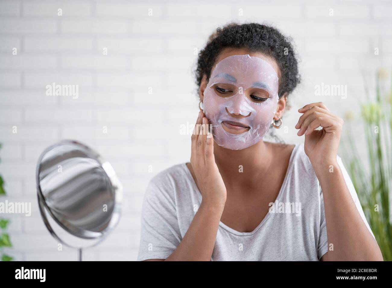 Femme appliquant le masque facial en papier tout en regardant dans le miroir à accueil Banque D'Images