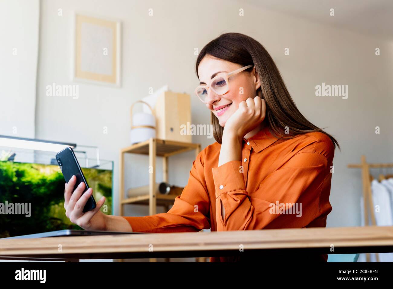Femme de mode travaillant à la maison assis au bureau avec smartphone Banque D'Images