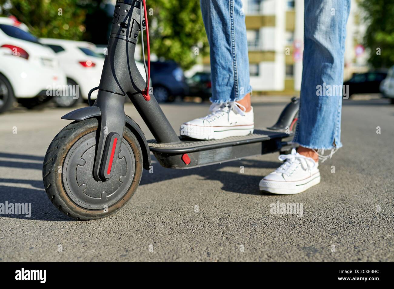 Femme debout avec un scooter électrique sur route sous le soleil jour Banque D'Images