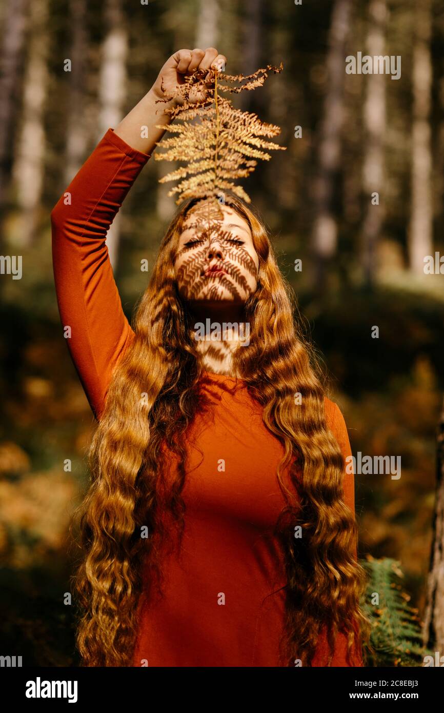 Belle femme avec de longs cheveux tenant les feuilles tout en restant debout forêt Banque D'Images