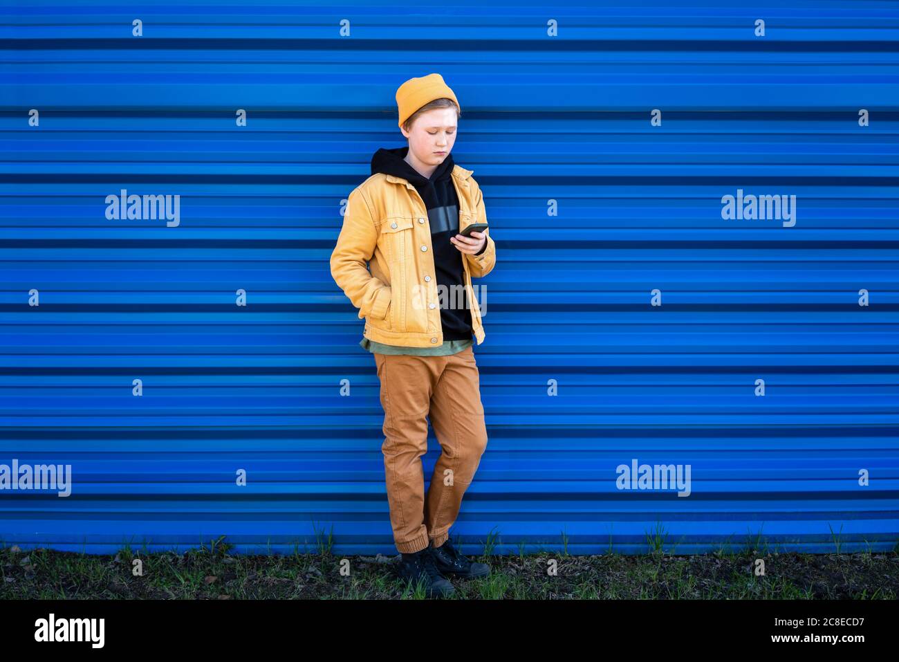 Garçon utilisant un smartphone tout en se tenant contre l'obturateur bleu Banque D'Images