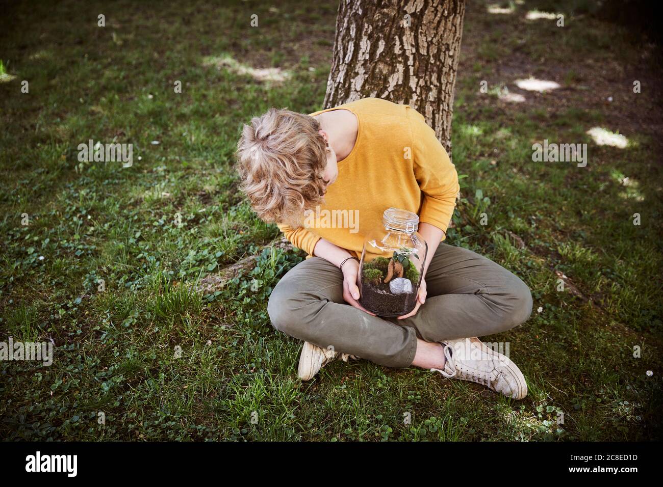 Jeune homme assis dans le jardin avec des plantes dans un verre Banque D'Images