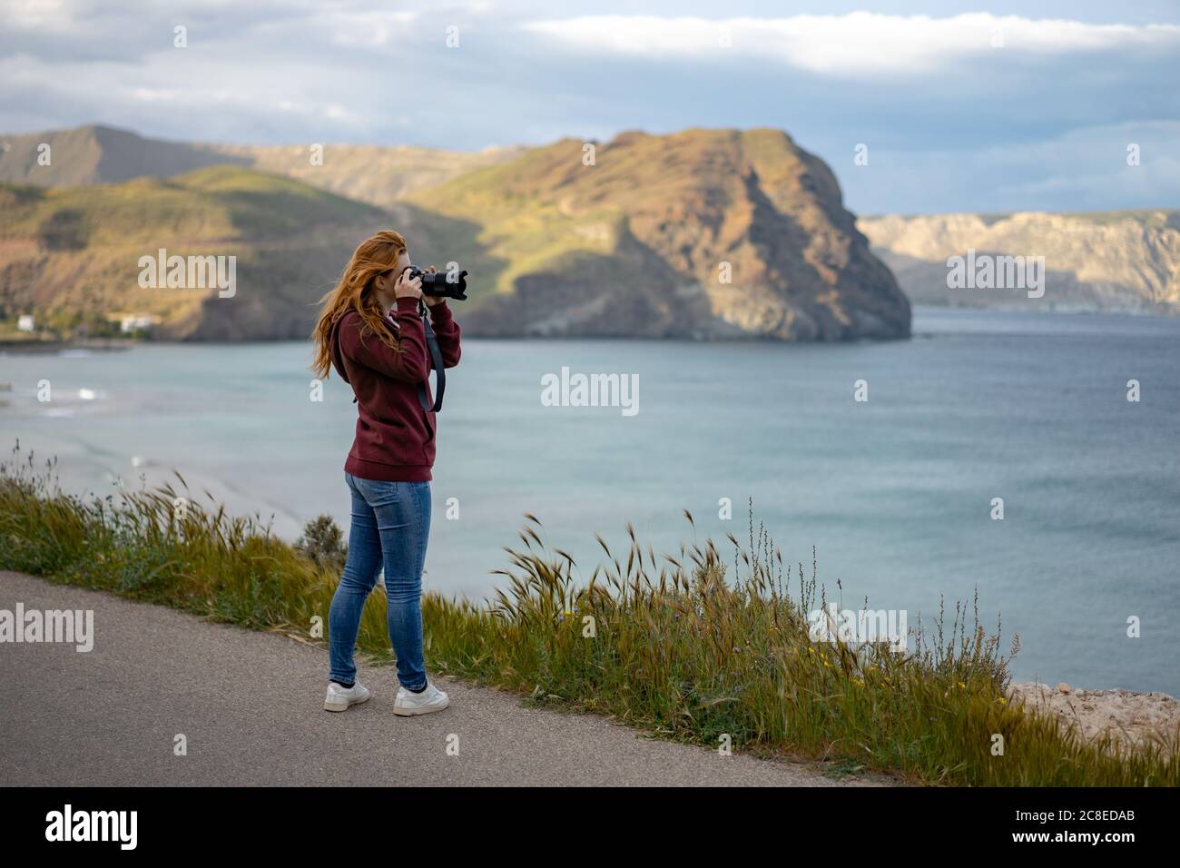Vue latérale d'une femme photographiant un paysage marin avec un appareil photo en montagne Banque D'Images