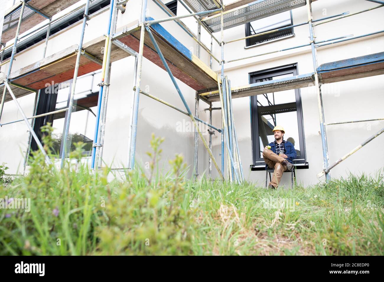 Travailleur de la construction réfléchi assis contre la maison sur le chantier de construction Banque D'Images