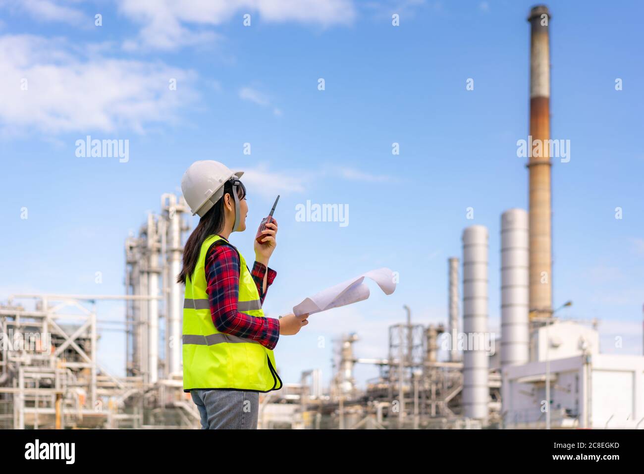 Femme asiatique technicien Ingénieur industriel utilisant walkie-talkie et tenant bluprint travaillant dans une raffinerie de pétrole pour l'étude de chantier de construction en ingénieur civil Banque D'Images