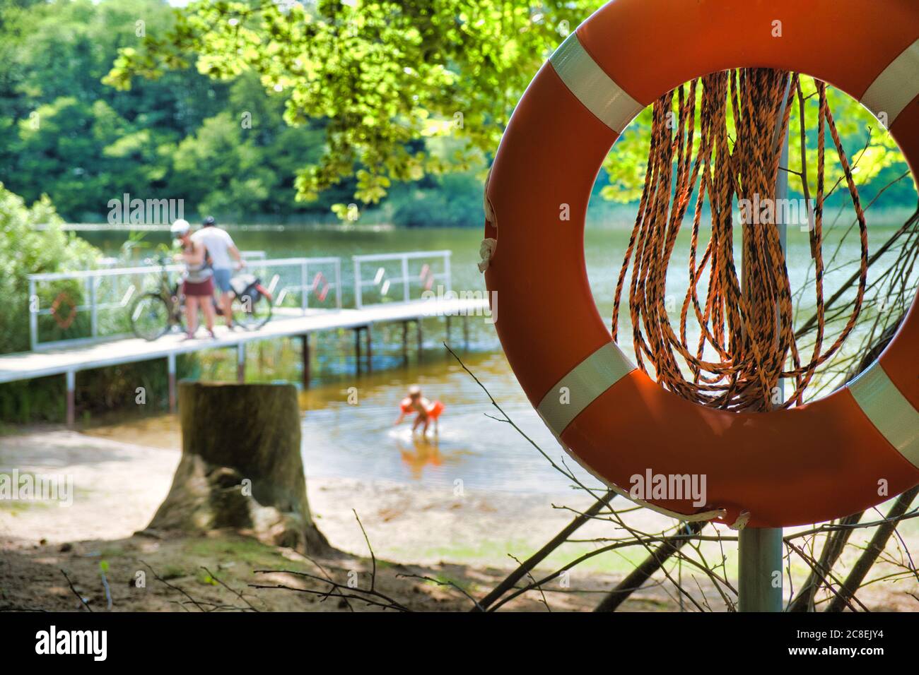 Sauvetage de la ceinture de sauvetage devant un lac et une passerelle en été. Des gens flous en arrière-plan. Banque D'Images