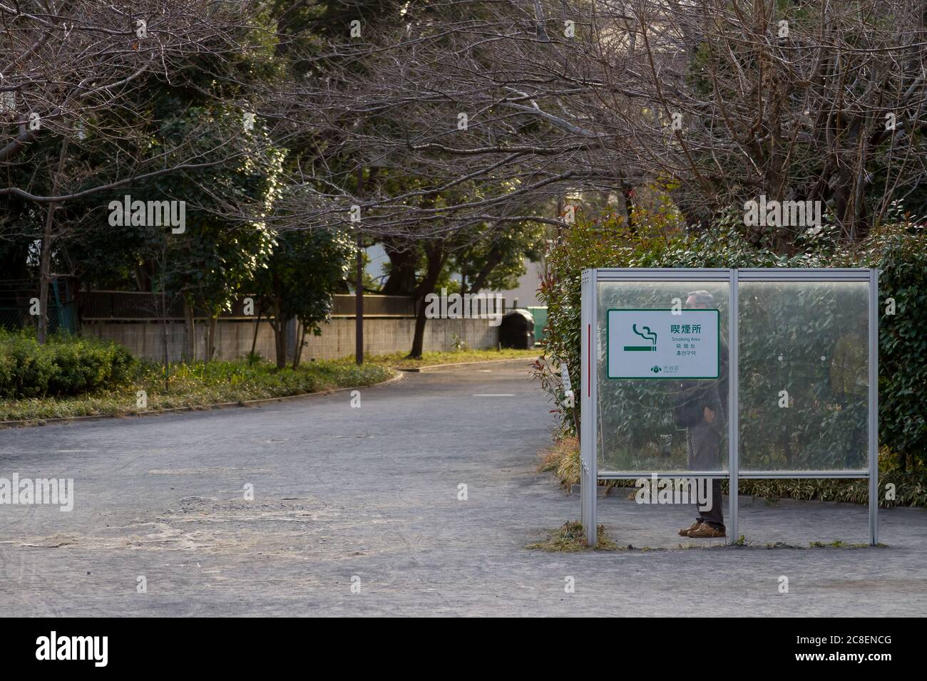 Un homme fume dans une zone fumeur à l'intérieur d'un petit parc à Shinjuku, Tokyo, Japon. Banque D'Images