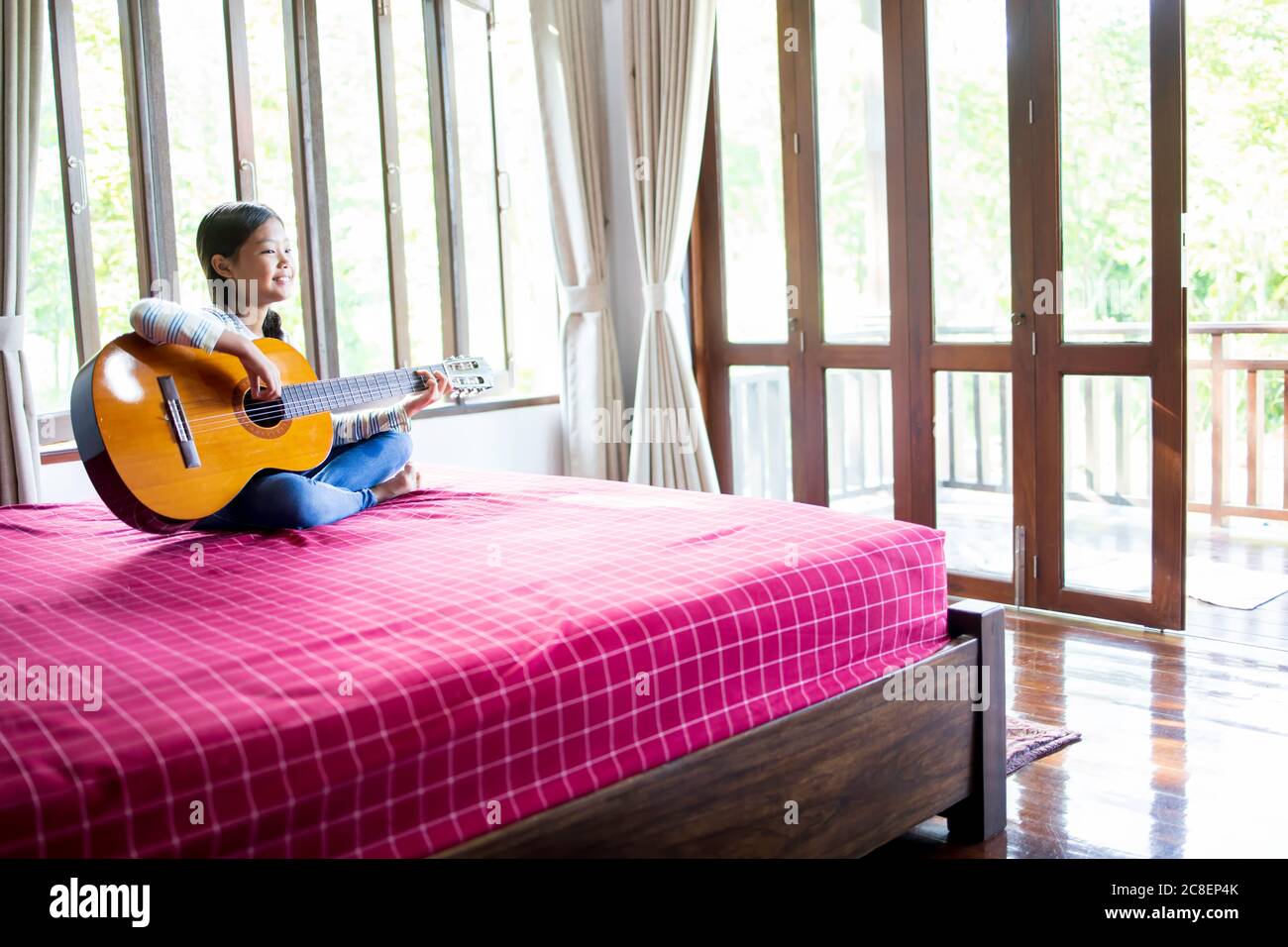 Une mignonne, fille d'école élémentaire asiatique à poil long, apprécie de jouer de la guitare dans sa chambre. Banque D'Images