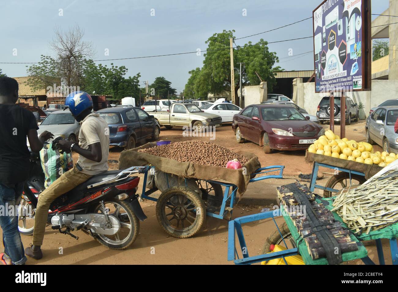 Poussettes de marchandises à vendre et voitures garées au bord d'une intersection très fréquentée à Niamey, Niger, Afrique Banque D'Images