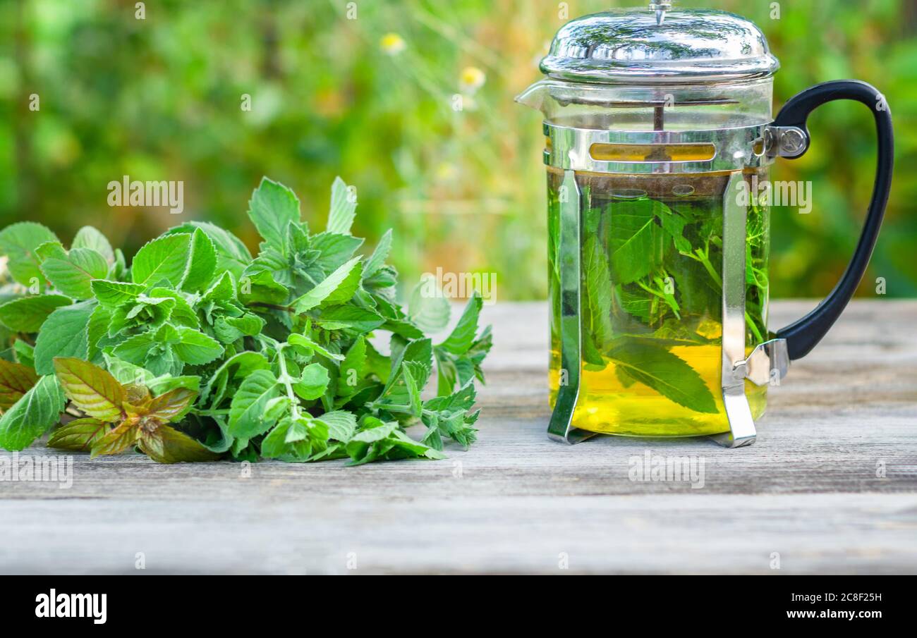 Composition de thé à la menthe fraîche dans une théière en verre sur une table en bois. Banque D'Images
