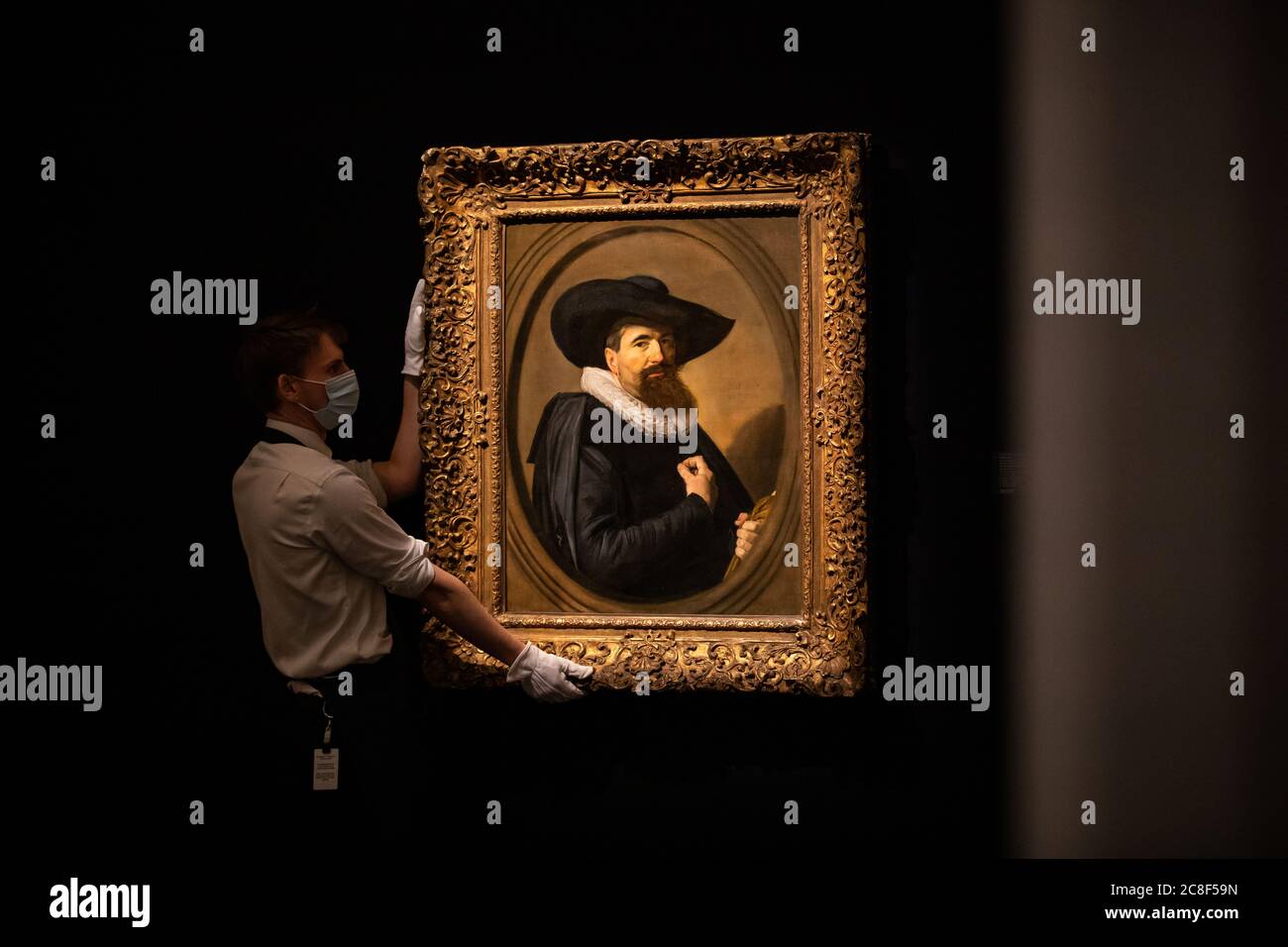 Un assistant de galerie pose à côté du portrait d'un homme, demi-longueur en noir avec un chapeau noir à large bord et une ruff blanche, tenant ses gants avec un ovale peint par Frans Hals, 1635, Huile sur toile avec une estimation de 2-3 millions de GBP lors d'un aperçu de presse à Sotheby's à Londres, avant leur vente de « Rembrandt à Richter » le 28 juillet. Banque D'Images