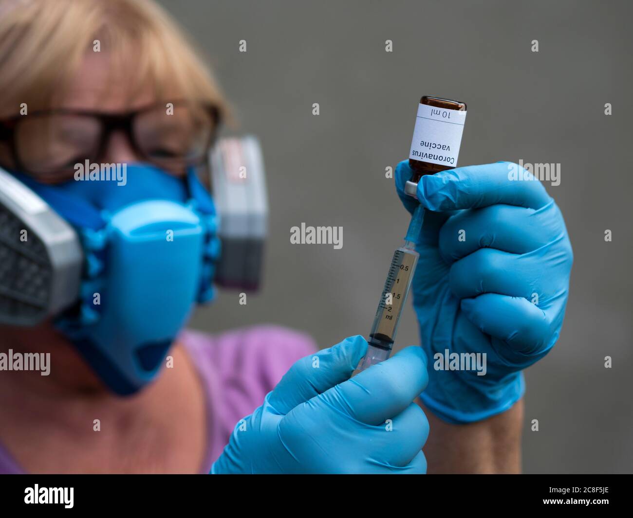 Dans cette photo avec foyer sélectif, un scientifique portant un respirateur à médiation et des gants en caoutchouc seringues liquide d'un flacon étiqueté Coron Banque D'Images