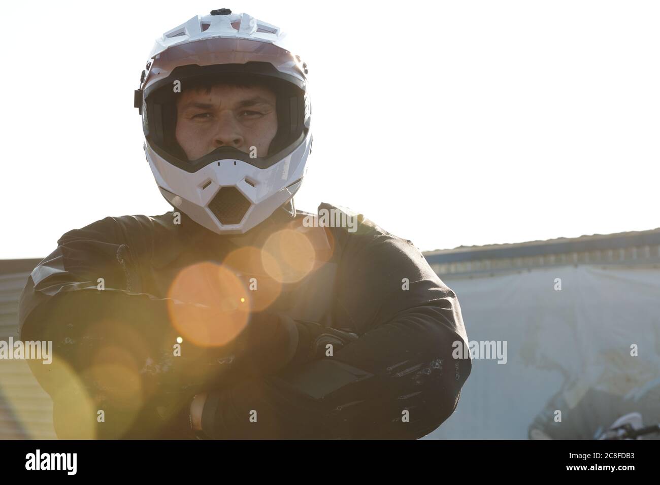 Portrait d'un automobiliste sérieux et confiant en port de protection et casque debout avec bras croisés à l'extérieur, effet de lumière du soleil Banque D'Images