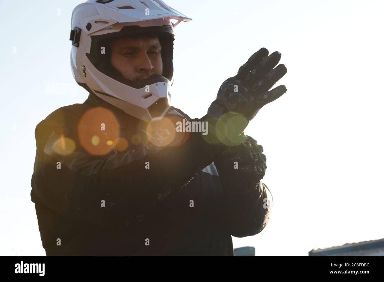Moto sérieuse dans le casque mettant des gants sur les mains tout en se préparant à la conduite à l'extérieur, effet de lumière de lentille Banque D'Images