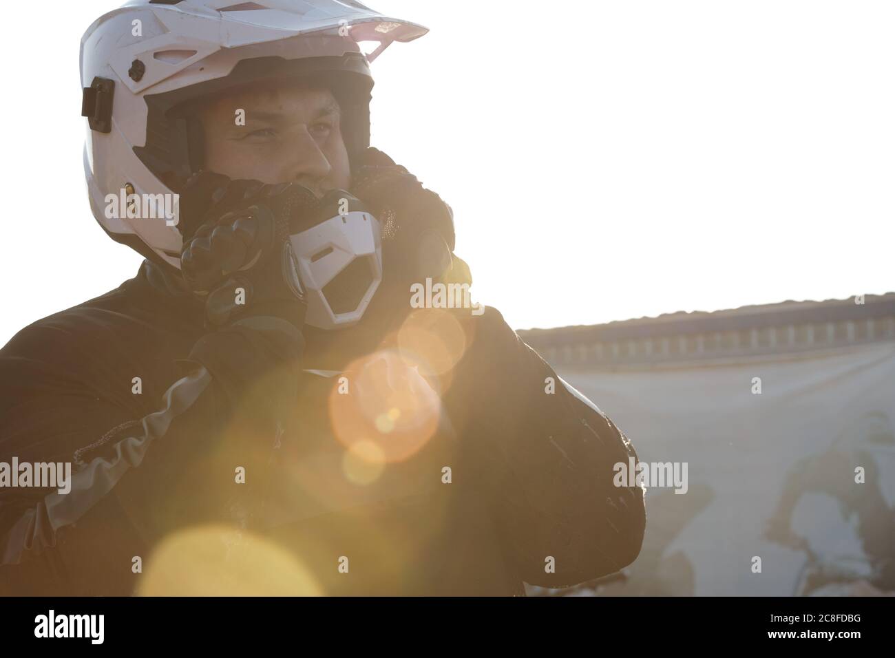 Motocycliste expérimenté en gants, ajustement du casque de moto à l'extérieur, effet de lumière de lentille Banque D'Images