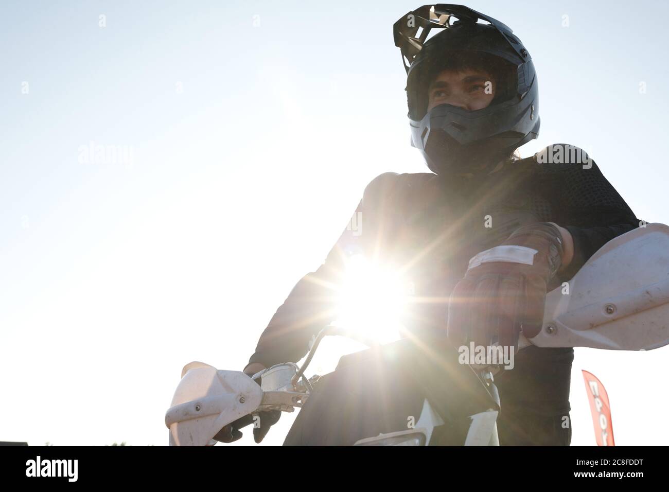 Vue ci-dessous d'un cycliste automobile homme sérieux et déterminé dans un casque et des gants, appuyé sur une moto au soleil Banque D'Images