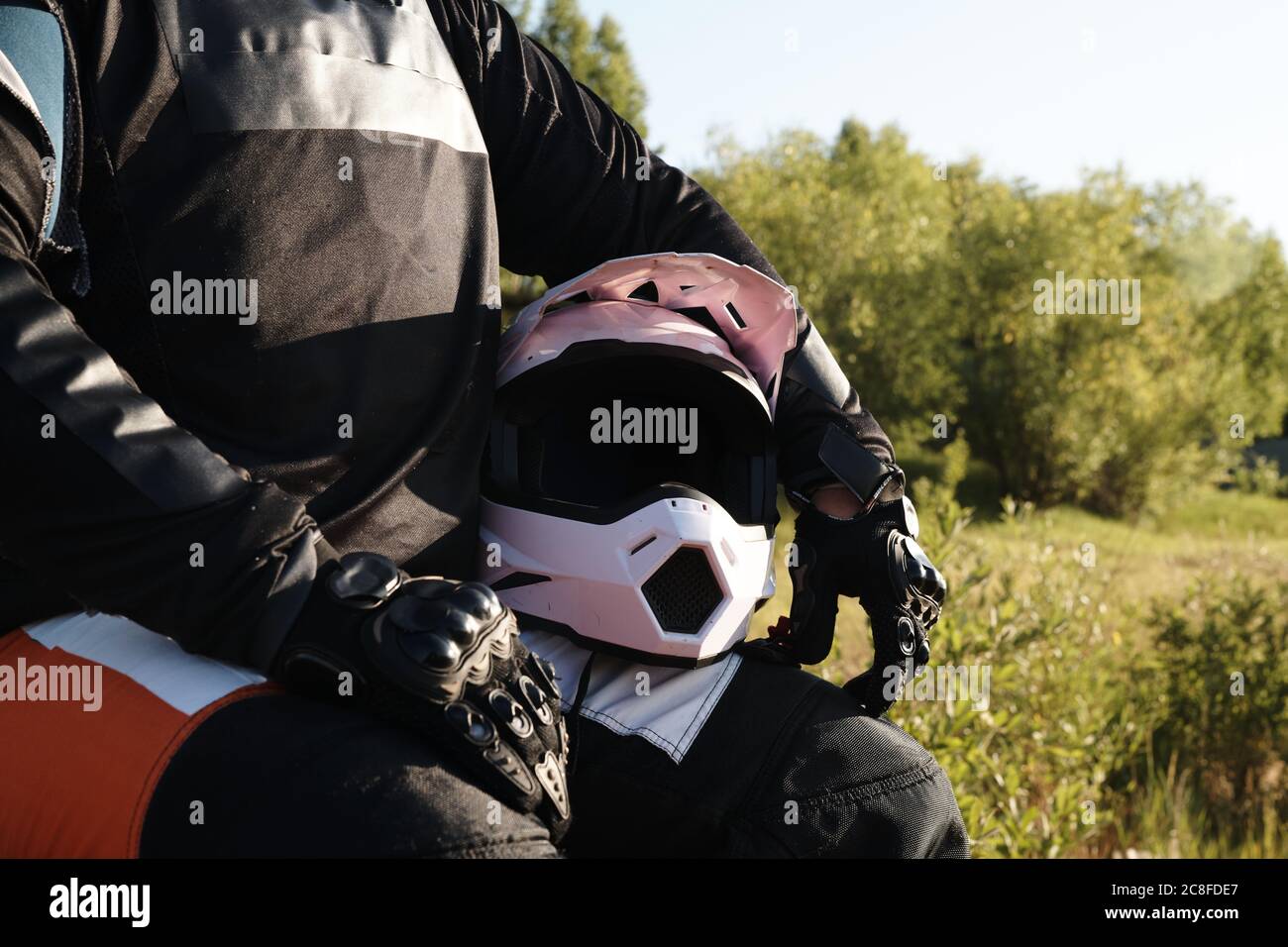 Gros plan d'un motocycliste méconnaissable en gants de protection assis avec un casque en forêt Banque D'Images