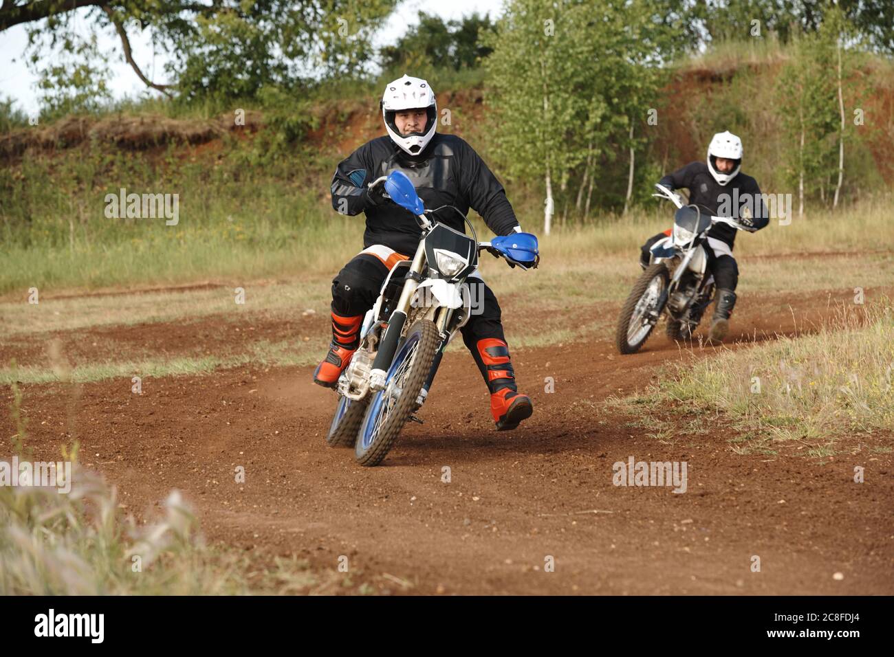 Hommes en tenues de protection appréciant le motocyclisme sur route sale tout en s'affrontant sur piste difficile Banque D'Images