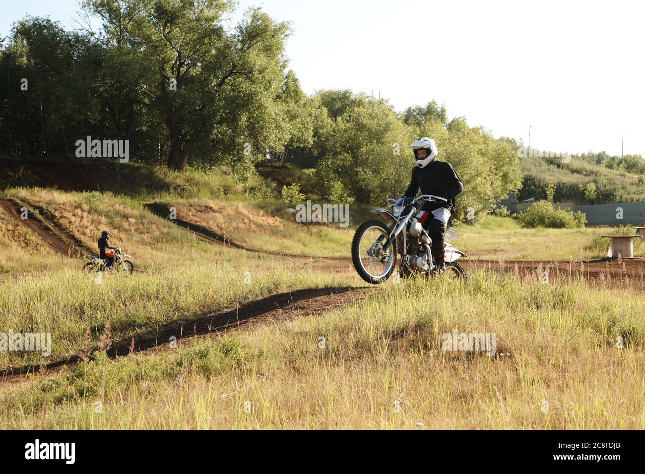 Homme en casque blanc qui roule en moto sur terrain accidenté tout en descendant une pente sur piste Banque D'Images