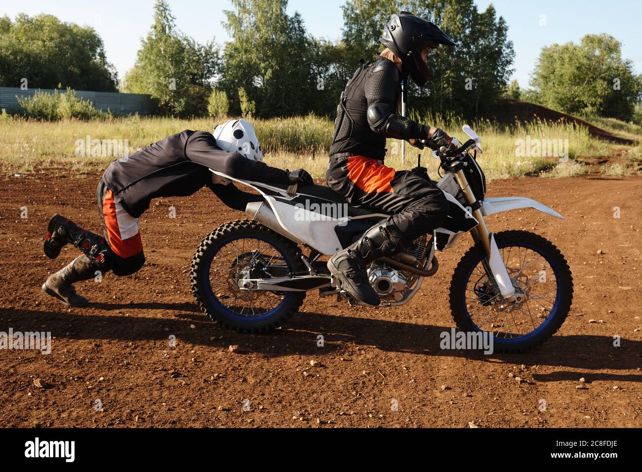 Motocycliste dans un casque poussant moto avec un ami pour le lancer sur une route accidentée Banque D'Images