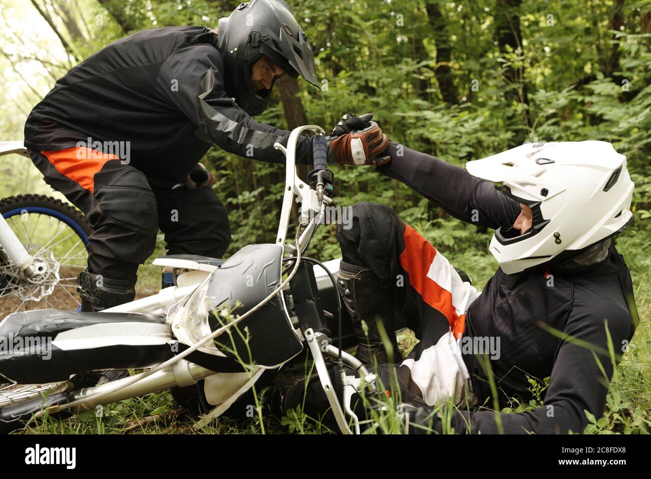 Motocycliste en casque aidant ami tombé hors de moto en forêt, amitié et de soutien concept Banque D'Images