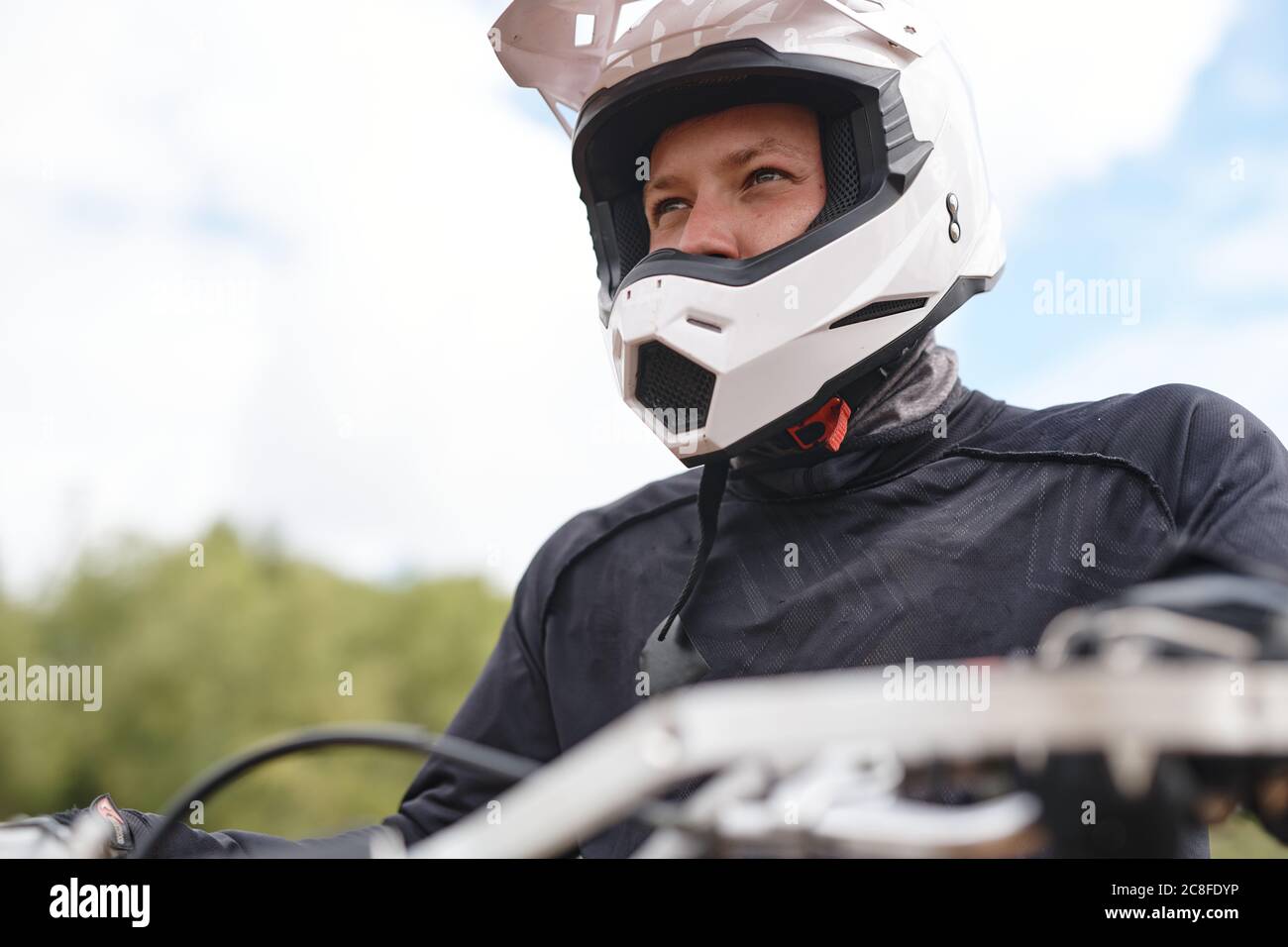 Déterminé motard dans casque blanc et veste assis sur moto et regardant à distance à l'extérieur Banque D'Images