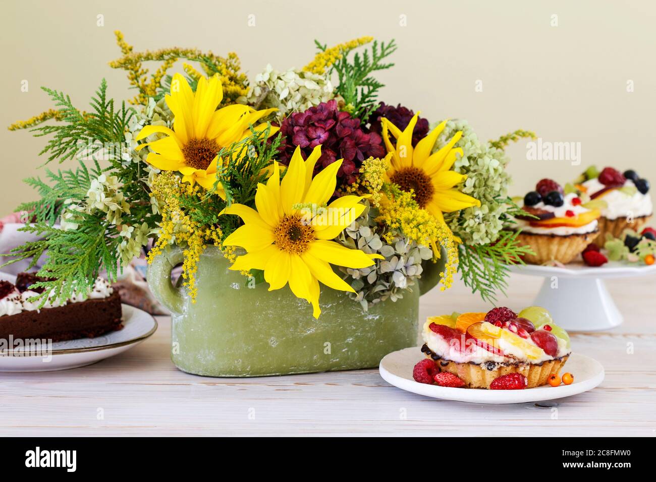 Petits gâteaux colorés et arrangements floraux avec tournesols et hortensias sur table de fête. Banque D'Images