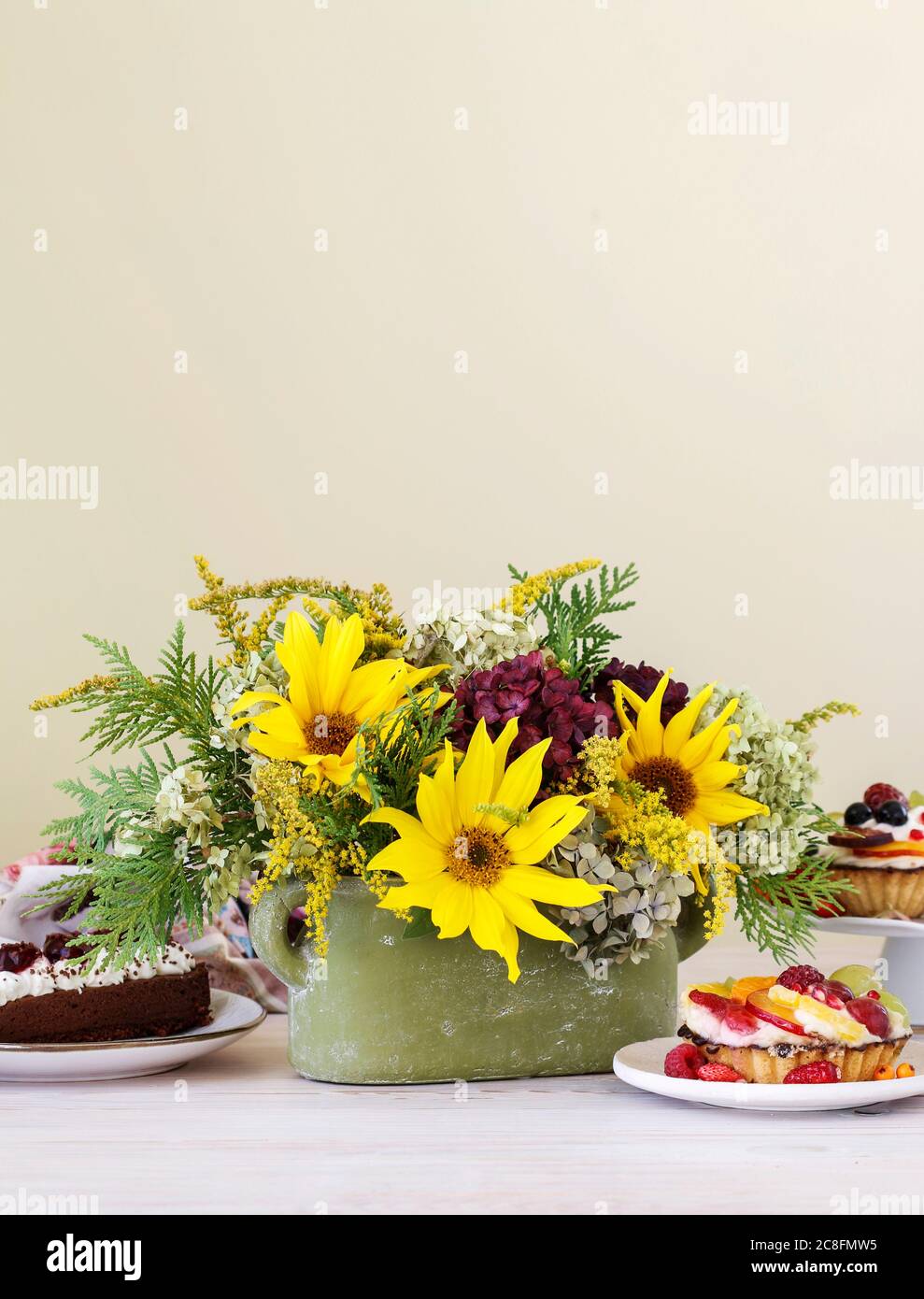 Petits gâteaux colorés et arrangements floraux avec tournesols et hortensias sur table de fête. Banque D'Images