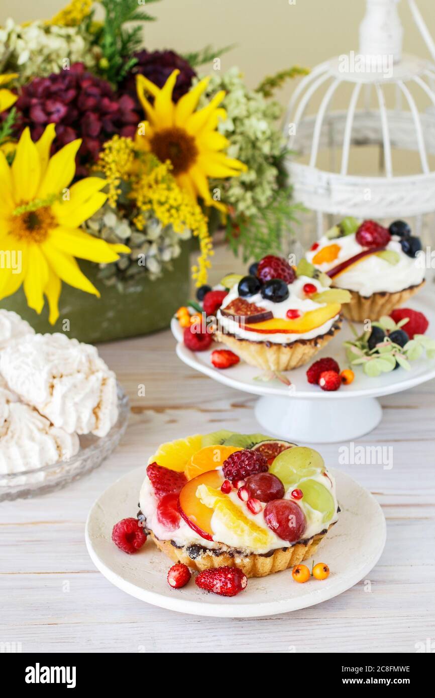 Petits gâteaux colorés et arrangements floraux avec tournesols et hortensias sur table de fête. Banque D'Images