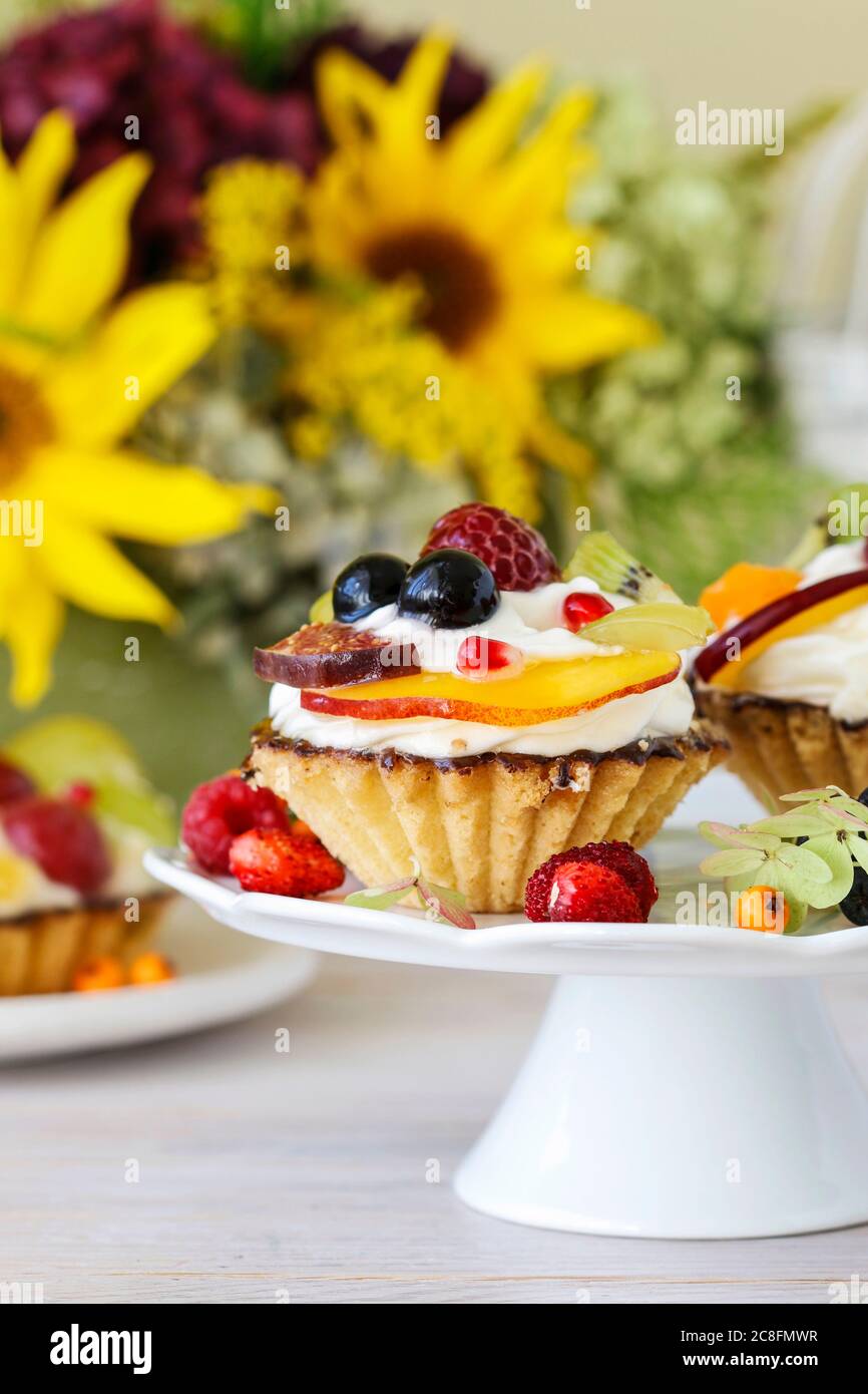 Petits gâteaux colorés et arrangements floraux avec tournesols et hortensias sur table de fête. Banque D'Images