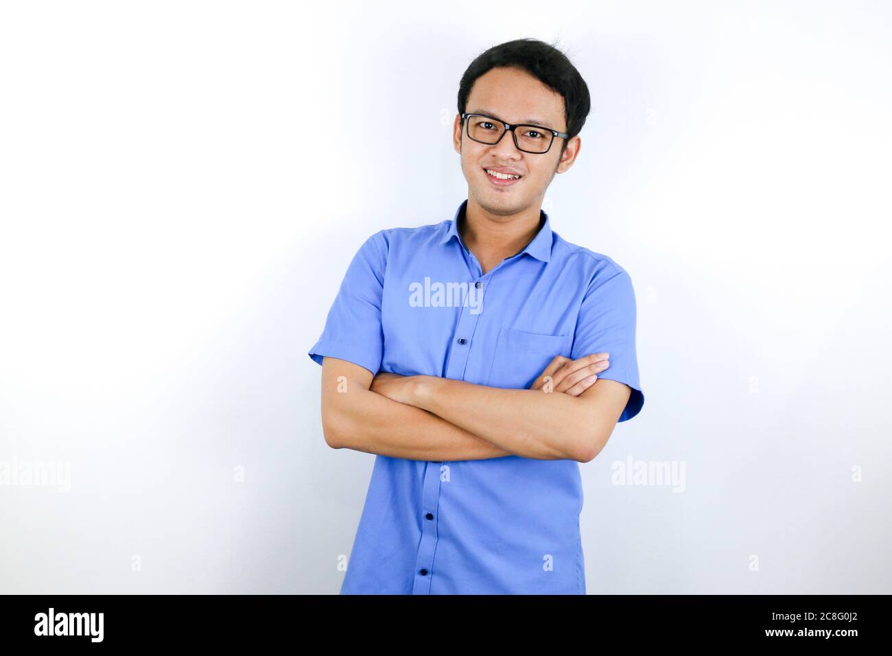 Portrait d'un jeune asiatique vêtu à la mode, debout avec confiance avec ses bras croisés contre un mur gris. Banque D'Images