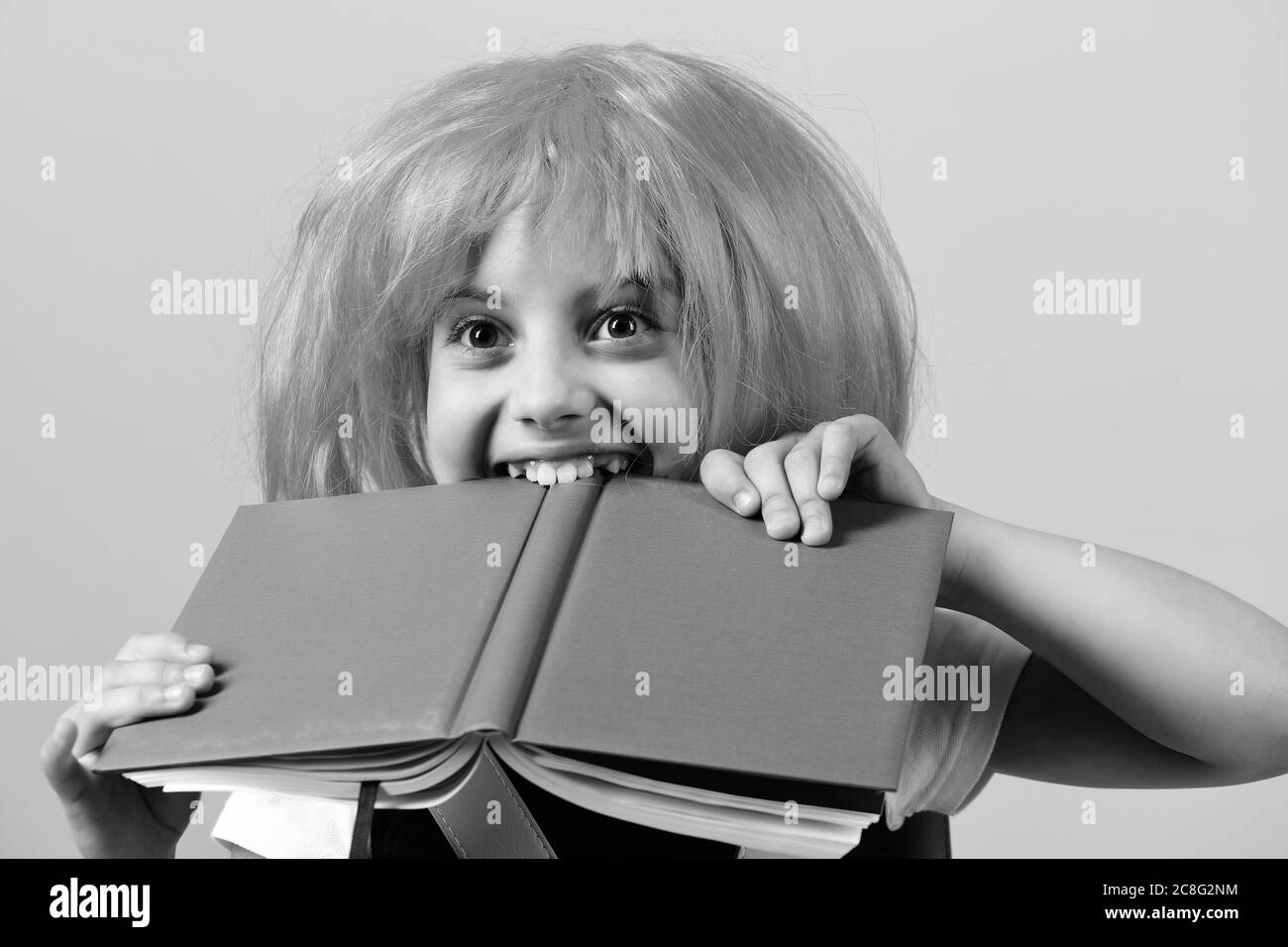 Fille morsures grand livre bleu. Fille d'école avec visage heureux isolé sur fond rose. Retour à l'école et concept d'éducation. Élève en uniforme scolaire avec perruque rose. Banque D'Images