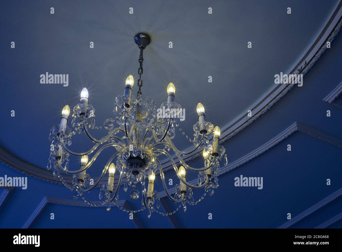 Comparaison des ampoules à économie d'énergie et des ampoules classiques dans un lustre en verre sous un plafond bleu. Banque D'Images